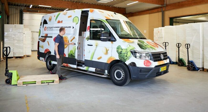 A man loading a van with produce in a warehouse, preparing for transportation.